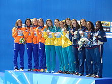 Links vier Niederländerinnen in oranger Trainingsjacke und blauer Hose mit ihrer Silbermedaille. Dann die siegreichen Australierinnen in grüner Trainingshose und grün-goldenen Jacken. Rechts im blauen Trainingsanzug das Quartett aus den Vereinigten Staaten.