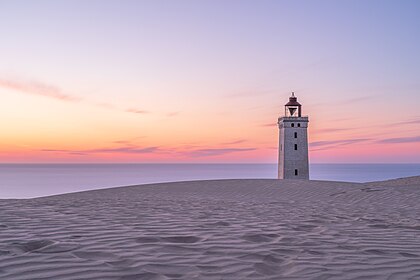 Rubjerg Knude Fyr, um farol construído em 1900 entre Lønstrup e Løkken na Dinamarca. A partir de 1910, o vento soprou grandes quantidades de areia das falésias, formando uma duna entre o farol e o mar. A duna se moveu para o nordeste e agora passou completamente pelo farol. Das dependências do farol só restaram tijolos soltos. É esperado que o farol venha abaixo em breve. As autoridades da natureza dinamarquesa planejam demolir o prédio antes que ele caia no Mar do Norte (definição 6 720 × 4 480)