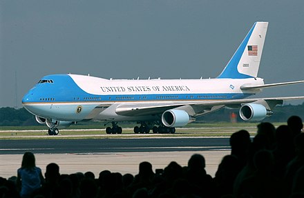 A Boeing 747 aircraft with livery designating it as Air Force One. The cyan forms, the US flag, presidential seal and the Caslon lettering, were all designed at different times, by different designers, for different purposes, and combined by designer Raymond Loewy in this one single aircraft exterior design.