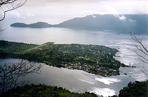 Blick von Banda Api auf Banda Neira mit dem Hauptort rechts und der Landebahn links. Im Hintergrund die Nachbarinsel Banda Besar.