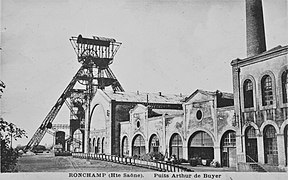 Photo noir et blanc de façades industrielles des années 1900 et grande tour triangulaire métallique à l'arrière plan.