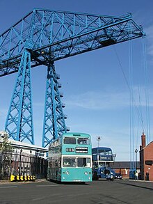 Preserved Teesside Municipal Transport L544, a 1972 Northern Counties bodied Daimler Fleetline CRL6, with Dennis Loline 99 in dark blue Middlesbrough Corporation livery at Middlesbrough Transporter Bridge Daimler Fleetline JDC544L at the Transporter Bridge.jpg