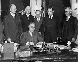 President Franklin Delano Roosevelt signs the bill into law in 1934. Standing behind him are (L-R): Henry Morgenthau Jr. (Treasury secretary), Eugene R. Black (Fed chair), George Warren (economist and advisor), Samuel Rosman and James Harvey Rogers (economist and advisor) Franklin Delano Roosevelt signs Gold Bill 1934.jpg