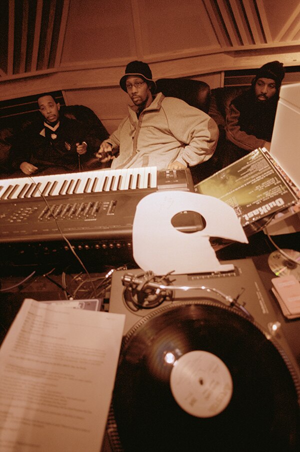 Hip hop producer and rapper RZA in a music studio with two collaborators. Pictured in the foreground is a synthesizer keyboard and a number of vinyl r