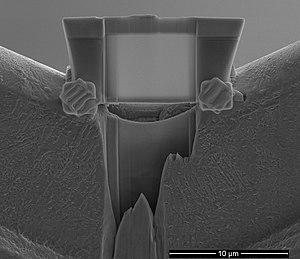 Vaheetapp läbivalgustava elektronmikroskoobi proovi valmistamisel, kus uuritavast objektist on ioonkiire abil välja lõigatud paari mikromeetri paksune ja paarikümne mikromeetri laiune lamell, mis on plaatinakontaktide (pildil nähtavad "lainelised" ruudud) abil vaskalusele kinnitatud (Markus Otsus)