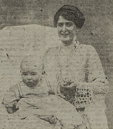 Black and white portrait of a dark haired women wearing a white dress holding a baby boy