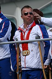 A man wearing sunglasses and a white and blue tracksuit with medals around his neck.