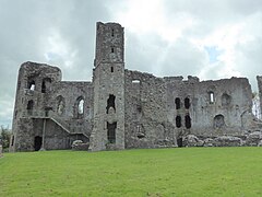 Photo d'un grand bâtiment en pierres grises, avec une grande tour, au milieu d'une pelouse verte