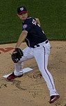 A man in a dark blue baseball jersey with a curly "W" on his cap throws a pitch.