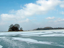 Mettnau und vorgelagerte Liebesinsel im Winter mit vereister Wasseroberfläche und Schlittschuhläufern (Februar 2006, Sichtrichtung Nordwesten); ganz im Hintergrund Radolfzell