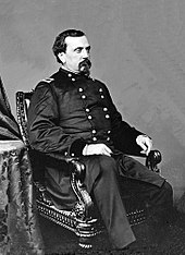 Photographie d'un homme moustachu et barbu en uniforme assis dans un fauteuil