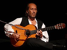 Fotografia de um homem sentado no palco, tocando violão