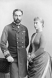 Fekete-fehér fénykép, amelyen egy tengerész egyenruhás szakállas férfi és egy ruhát viselő nő látható, háromnegyedes kilátással.