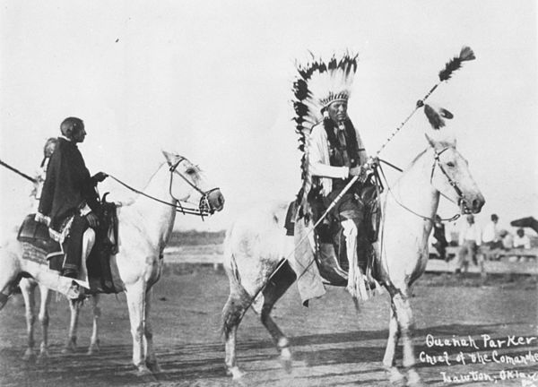 Quanah Parker on horseback wearing eagle feather headdress and holding a lance bottom-up.