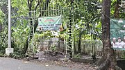 An open entrance to the area of the urban farm designated with a hanging tarpaulin sign, located along a concrete road.