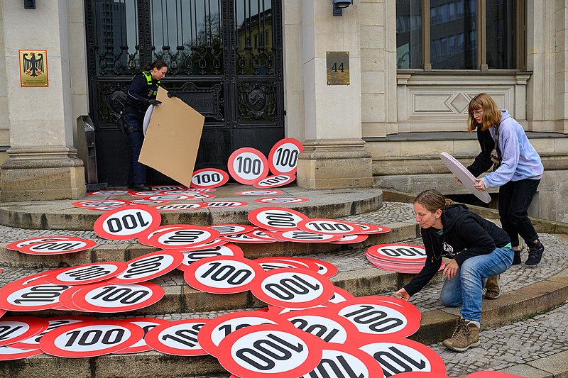 File:Aktivistinnen vom Aufstand der Letzten Generation räumen gemeinsam mit Polizei Tempo-100-Schilder vor dem Verkehrsministerium auf. (52446029228).jpg