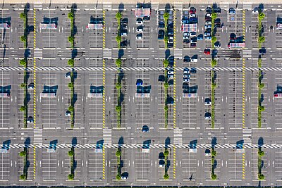 Top view of a gray concrete surface with some cars and shelters.  Several streets running horizontally are marked with white paint on the concrete surface, with smaller tramlines in between like the rungs of a ladder.  A row of parking areas, a narrow green strip and again parking spaces are arranged between the tramlines.  In some places there are white hatched areas for pedestrian traffic.