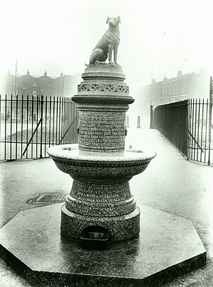 Photograph of a circular fountain with a dog at the top in stone