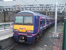 A purple colour train parked on a platform. The name of the company i.e. "First" is written on the sides. The last coach has a yellow paint on lower half with "first" and logo "f" written on it. It also has number 322 485 written on it.