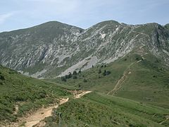 Alpages traversés par un sentier de randonnée se prolongeant en zigzag jusqu'à une crête.