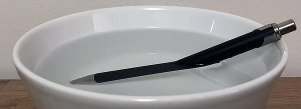 A pen partially submerged in a bowl of water appears bent due to refraction at the water surface.