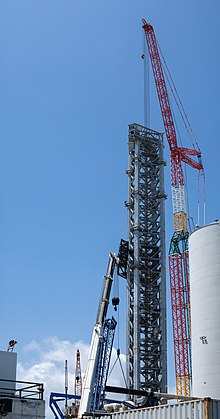 A tall stell white launch tower with a platform on top