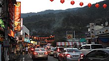 City street with heavy traffic, orange overhead lanterns, and mountains in the background