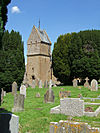 Building with square tower. In the foreground are gravestones.