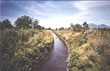 Photo d'une rivière traversant un milieu végétal avec des montagnes en arrière-plan