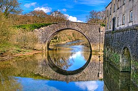 Un vieux pont à une arche se reflétant dans la rivière longeant un bâtiment.