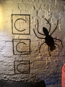 A painting of a spider with the letters "C C C" next to it on a wall