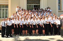 Foto der letzten Schülerklasse in blauen Uniformen und weißen Hemden vor dem Forschungsgebäude mit der Schulleitung