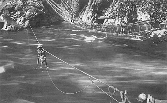 A passenger traversing the river precariously seated in a small suspended cradle Circa 1900