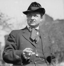 A black and white photograph of a man wearing a suit and hat, with a cigarette in his hand.