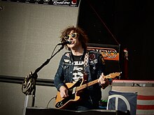 Un uomo con una camicia di jeans che canta in un microfono mentre suona la chitarra
