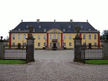 Une porte en fer s'ouvre sur un palais rectangulaire de deux étages avec de grandes ailes attachées.  Fenêtres en plein cintre et pierre apparente à l'entrée et au deuxième étage des ailes.