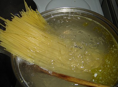 Spaghetti being placed into a pot of boiling water for cooking