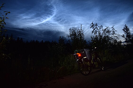 Bike and noctilucent clouds, in a dark forest