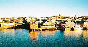Un groupe de bâtiments et de quai, avec un petit navire amarré sur la droite de l'image. Les bâtiments situés au bord de l'eau se reflète dans la mer.