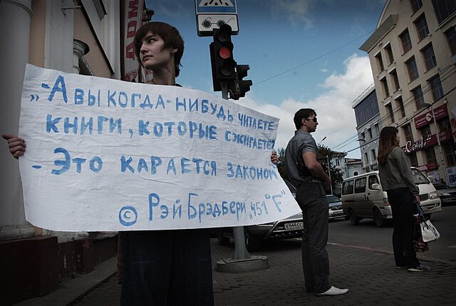 A protester against the Bhagavad Gita trial in Russia showing a quote from the novel: "– Do you ever read any of the books you burn? – That's against 