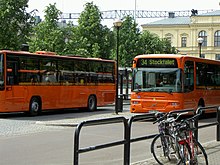 Charakteristische orange Busse im Karlstädter Linienverkehr. Hier sind zwei Busse am zentralen Wechselpunkt, dem Stora Torget, zu sehen. Dahinter erkennt man das Rathaus von Karlstad mit Räumlichkeiten für das wärmlandische Landgericht und das Berufungsgericht für Westschweden.