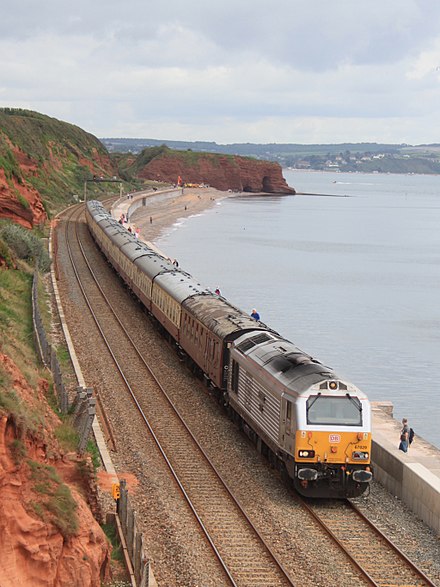 Train departs Dawlish on the Riviera Line, travelling along sea wall.