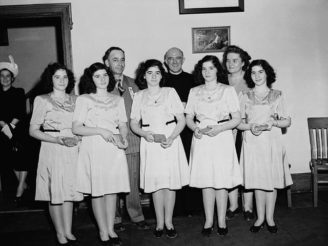The quintuplets in 1947 with their parents and a priest in the background