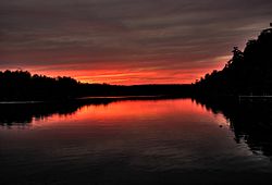 Лесистые берега озера на фоне темно-красного неба