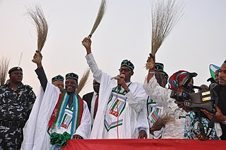 Generaal Buhari houdt een bezem vast tijdens een campagnebijeenkomst.jpg