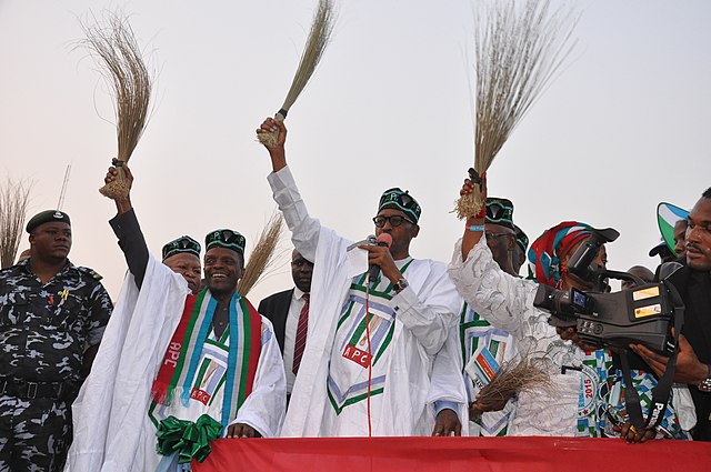 Nigerian opposition politicians holding brooms at a campaign rally