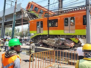 One of the railcars is being lifted by a crane. Behind it, the second railcar still hanging. Below them, a car is seen below the debris.