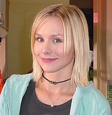 Head and shoulders shot of wide-eyed, young blond woman smiling into the camera.left