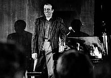 Martial Solal sur scène, souriant debout à côté de son piano en 1998. Il porte une chemise et une veste. On devine les têtes du public au premier plan. La photo est en noir et blanc.