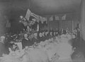 Men sitting around a long banquet table with American flags hanging above them, June 6, 1905 (PEISER 172).jpg